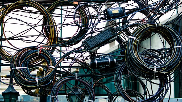 Intricate network of tangled power and communication cables outdoors.