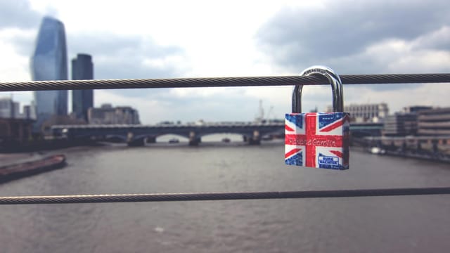 A colorful Union Jack padlock adorning bridge railings with London's skyline in the background.