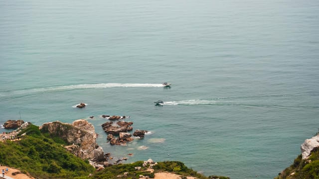 A tranquil aerial shot of boats navigating the ocean near the rocky coastline of Shenzhen, China.