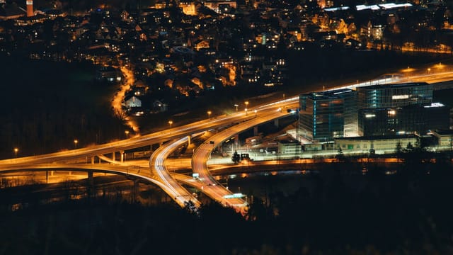 Highway curves through a lit cityscape at night, showcasing vibrant urban life.