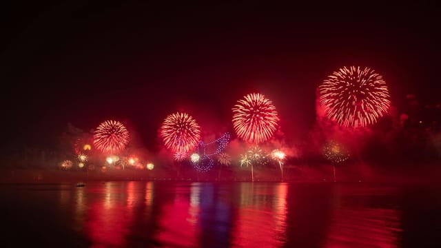 Dazzling fireworks illuminating the night sky over Ras al Khaimah, UAE, reflected in a calm lake.