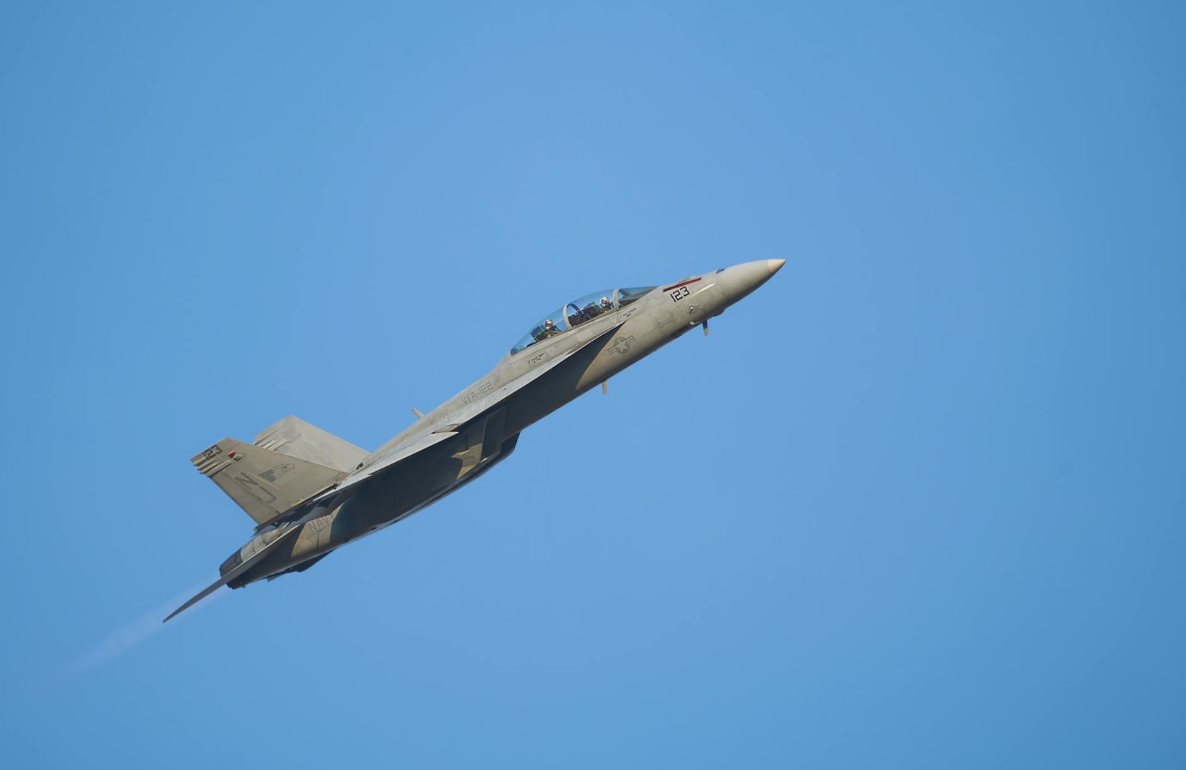 A military fighter jet ascending against a clear blue sky, showcasing power and precision.