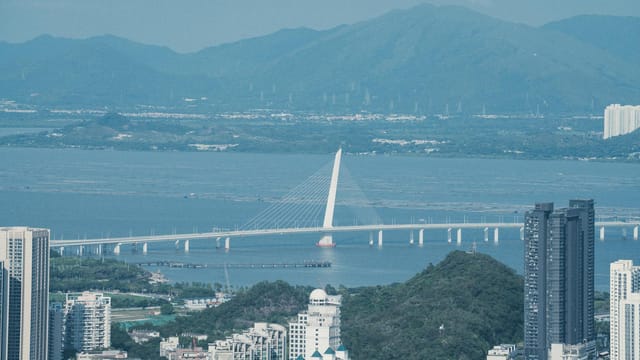 Captivating aerial view of Shenzhen Bay Bridge with towering skyscrapers and mountain backdrop.