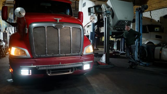Red truck in a garage with mechanic and elevated vehicles undergoing maintenance.
