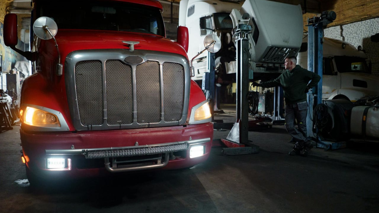 Red truck in a garage with mechanic and elevated vehicles undergoing maintenance.