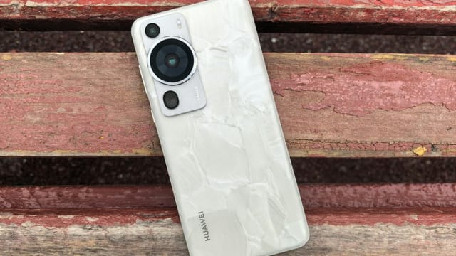 Modern smartphone with a textured back cover lies on a rustic wooden bench outdoors.