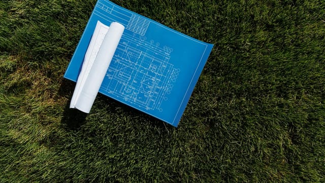 Top view of architectural blueprints on a grassy field, ideal for construction themes.