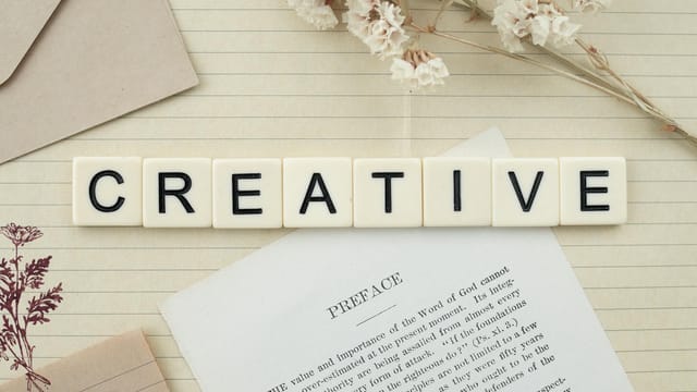 Close-up of letter tiles spelling 'Creative' on a lined notepad with decorative elements.