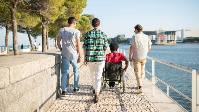 Four friends enjoying a sunny day by the seaside, with one using a wheelchair, in Portugal.
