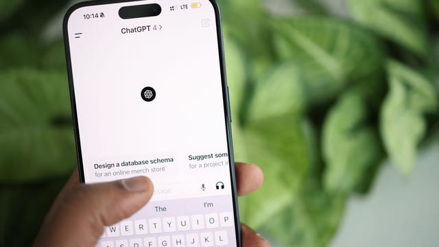 Hand holding smartphone displaying ChatGPT interface, surrounded by greenery.