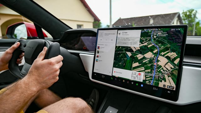 Man driving Tesla using GPS on touchscreen dashboard for navigation.