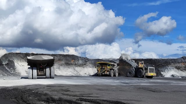 Open-pit mine with large trucks and excavators under blue sky.
