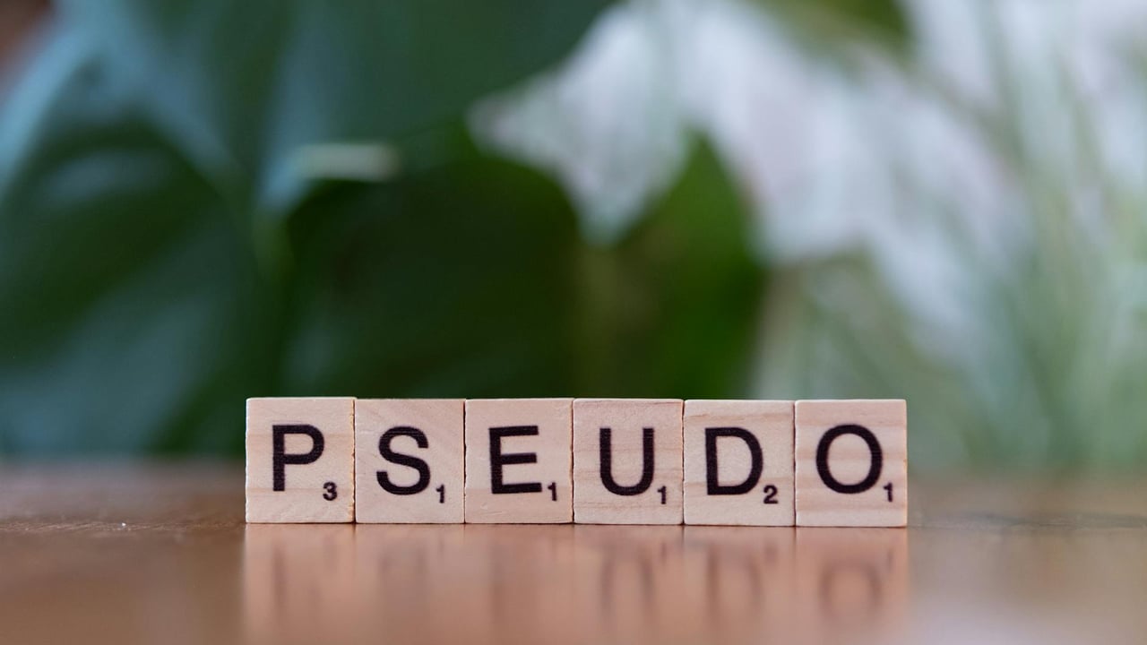 Wooden Scrabble tiles spelling 'Pseudo' on a reflective surface with a blurred green background.