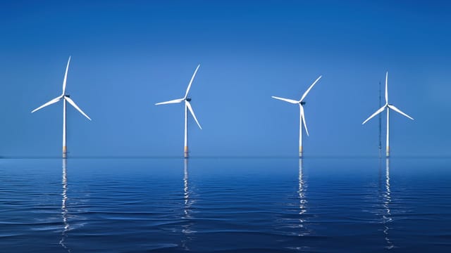 Serene landscape of offshore wind turbines reflecting on calm ocean water.
