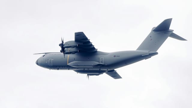 A military transport plane with propellers flies in the overcast sky, showcasing modern aviation technology.