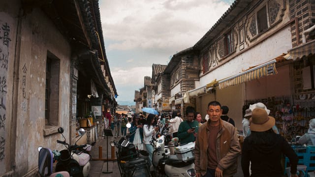 Vibrant outdoor market scene with people and scooters in a historic Asian street.