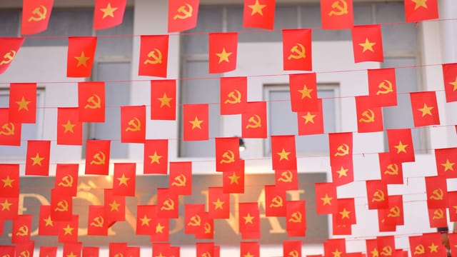 Multiple red flags with hammer and sickle symbols hang in a festive outdoor setting.