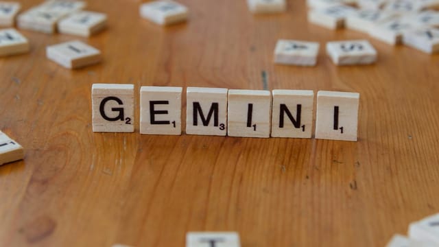 Gemini zodiac sign spelled with Scrabble tiles on a wooden table.