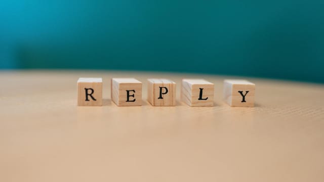 Close-up of wooden blocks spelling 'REPLY' on a table with teal background.