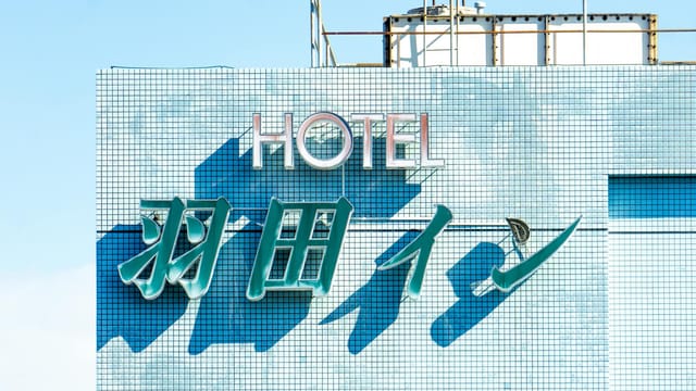 Brightly lit hotel sign with blue tiles under a clear sky, showcasing modern architecture.