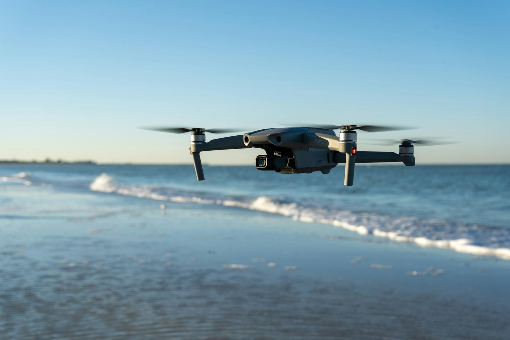 A drone flying over a tranquil beach with gentle waves in the background during sunset.
