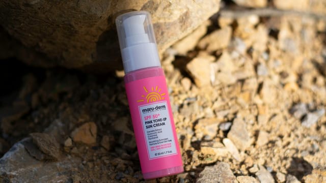 Close-up of SPF 50+ sun cream bottle with pink toned packaging on rocky surface.