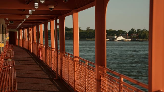 Empty Staten Island Ferry deck with scenic water view during sunset in New York City.