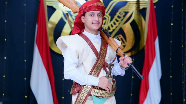 Man in traditional Yemeni attire with rifle, cultural background.