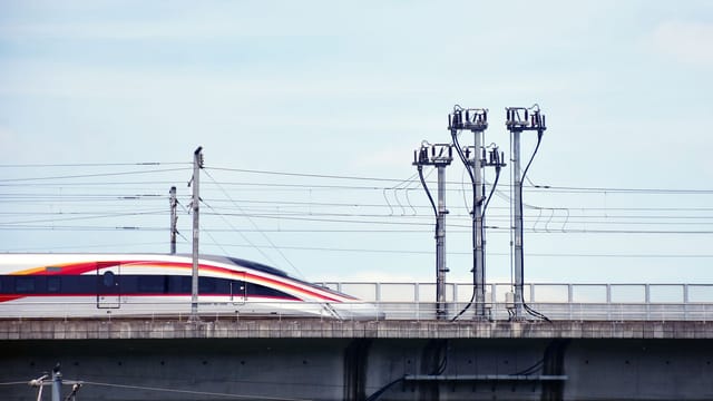 A high-speed train moves swiftly on an elevated railway under a clear sky.