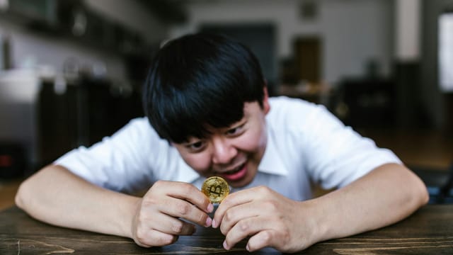 A young man excitedly examining a Bitcoin coin in an indoor setting.