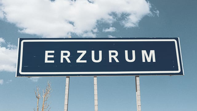 Street sign for Erzurum against a backdrop of a bright blue sky and fluffy clouds.