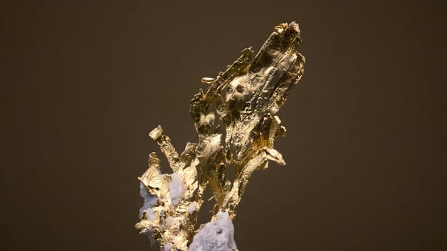 Close-up macro photograph of a striking gold mineral formation on a dark background.