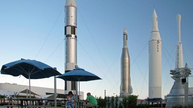 A couple sits under umbrellas with NASA rockets in the background.