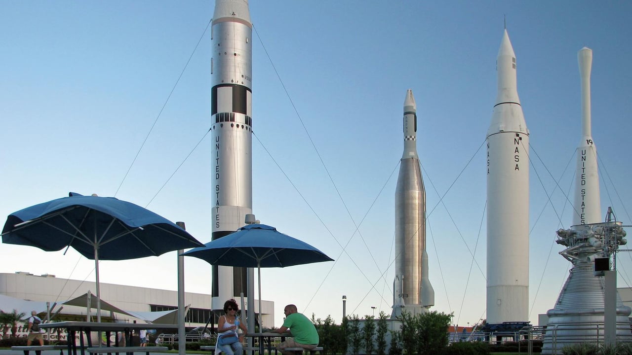 A couple sits under umbrellas with NASA rockets in the background.