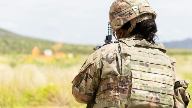 A soldier in a ballistic vest and camouflage uniform training outdoors at Fort Bliss.