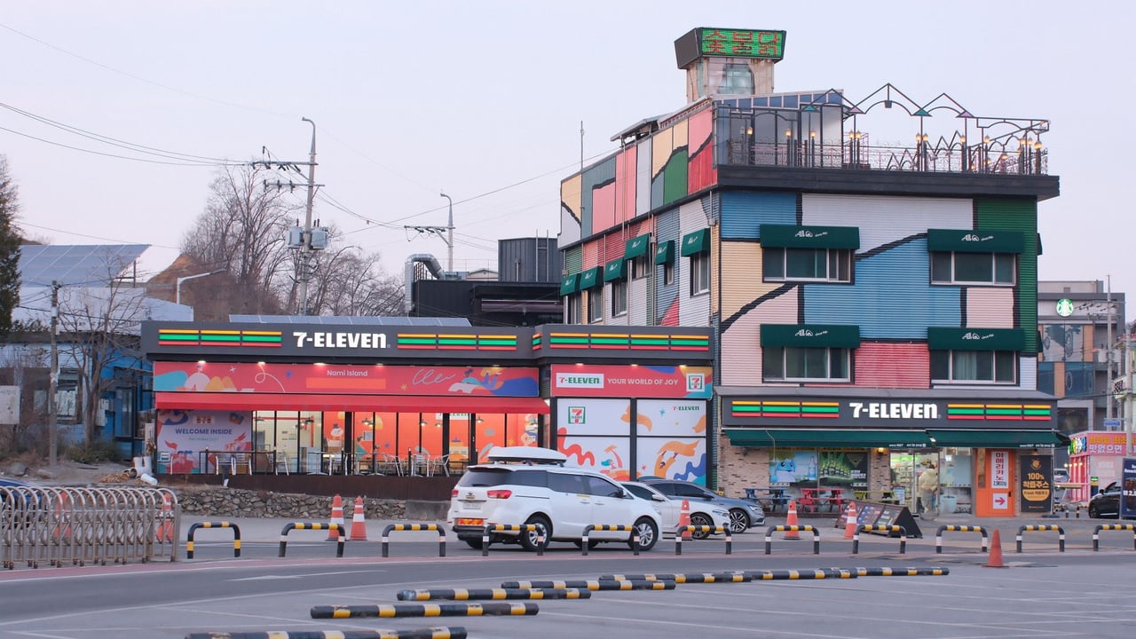 A vibrant 7-Eleven store with colorful facade and parking lot in the foreground, during daytime.