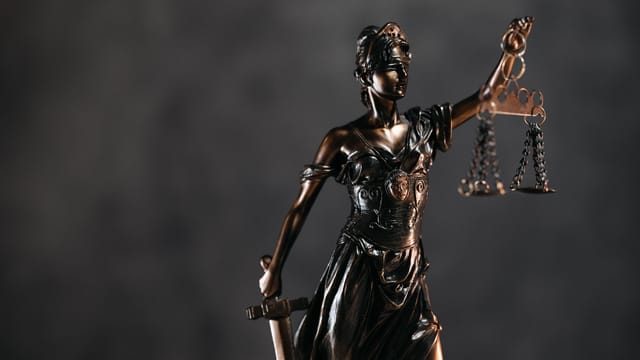 Detailed bronze Lady Justice statue with scales and sword against a dark background, symbolizing law and justice.