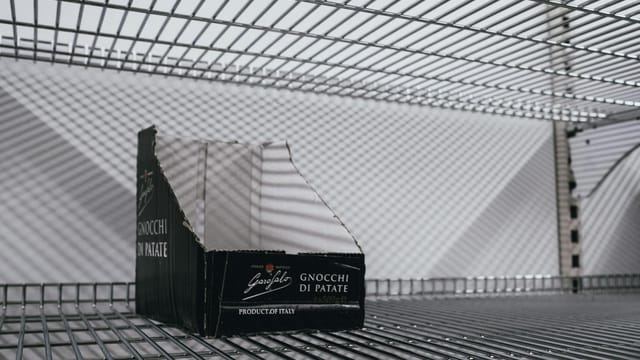 An empty supermarket shelf with an Italian gnocchi box symbolizing scarcity.