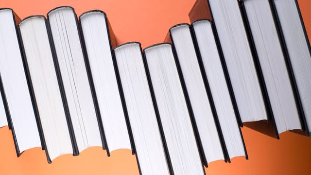 Stack of black hardcover books aligned against a vibrant orange backdrop, viewed from above.
