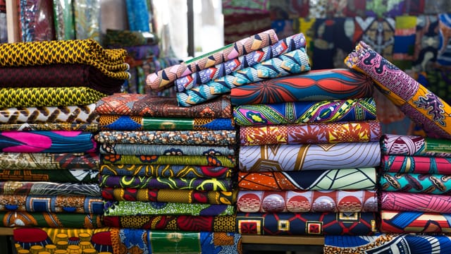 Vibrant stack of African fabrics at a market in Cotonou, showcasing bold patterns and colors.