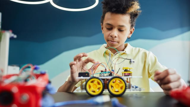 Boy explores robotics with toy vehicle and wires in a classroom setting.