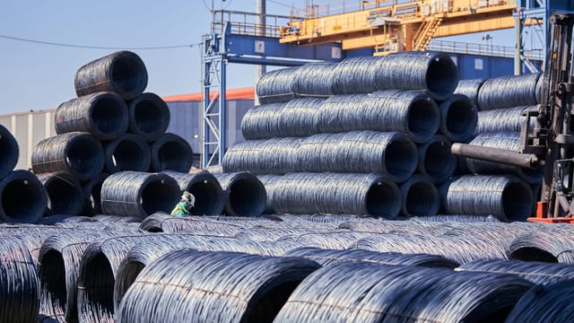 Large stacks of steel wire coils stored outdoors at an industrial site under bright daylight.