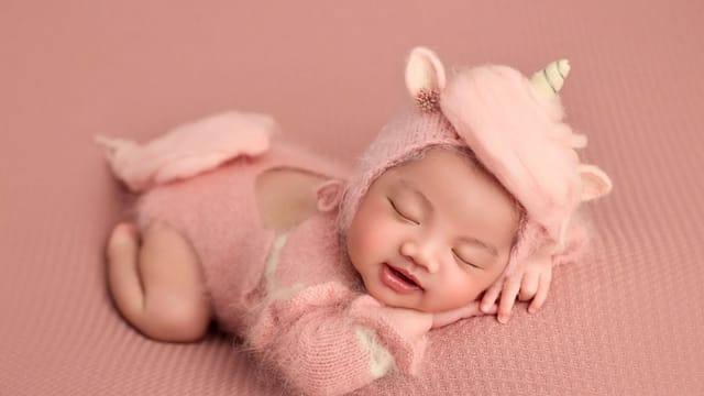 A cute baby dressed in a pink unicorn outfit sleeping on a soft pink background. Perfect for baby-themed projects.