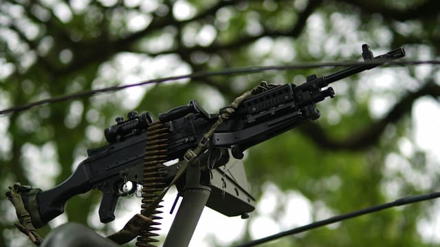 Close-up of a mounted machine gun outdoors with blurred trees.