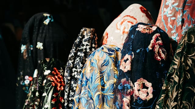 A colorful array of luxurious, embroidered fabrics displayed in a marketplace, showcasing intricate patterns.