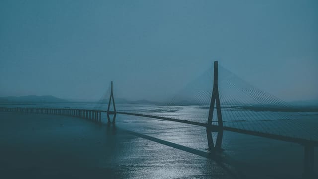A suspension bridge spans over calm waters under a moody sky in Fujian, China.