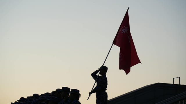 A soldier salutes with a flag during a parade at sunset, creating a striking silhouette.