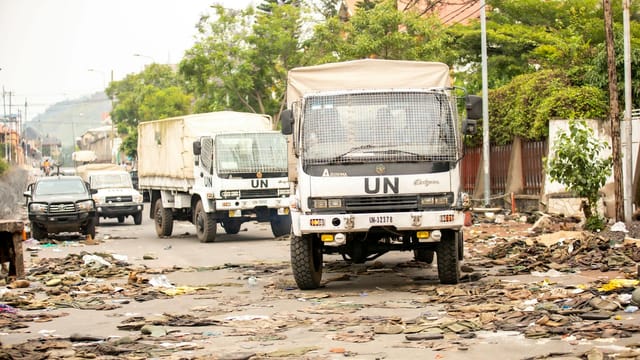 UN trucks travel through a debris-filled street, highlighting urban challenges.
