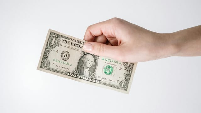 Close-up of a hand holding a one US dollar bill against a white background. Ideal for finance-related themes.