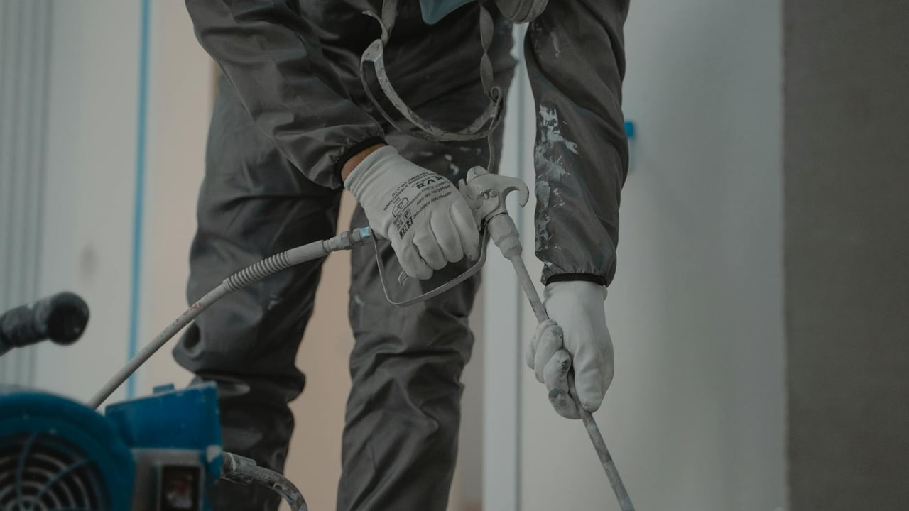 Worker in protective gear using a power spray for indoor renovation.